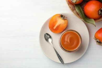 Photo of Delicious persimmon jam in glass jar served on white wooden table, flat lay. Space for text