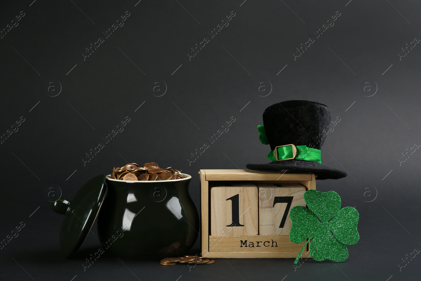 Photo of Composition with pot of gold coins and wooden block calendar on black background. St. Patrick's Day celebration