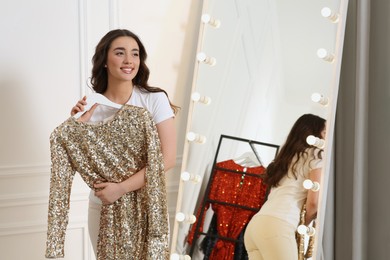 Beautiful young woman with golden sequin dress near mirror in boutique. Choosing party clothes