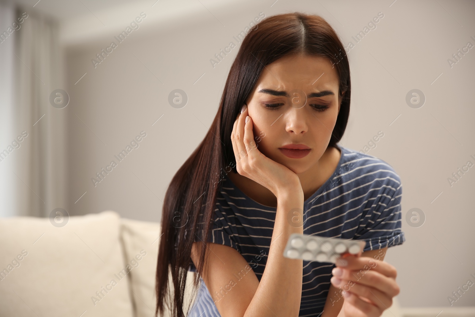 Photo of Confused young woman holding package of pills indoors