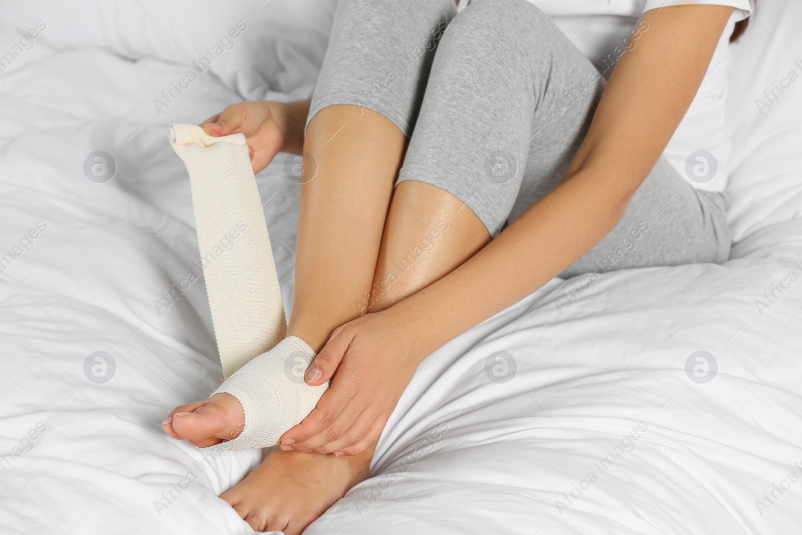 Photo of Young woman applying medical bandage onto foot on bed, closeup