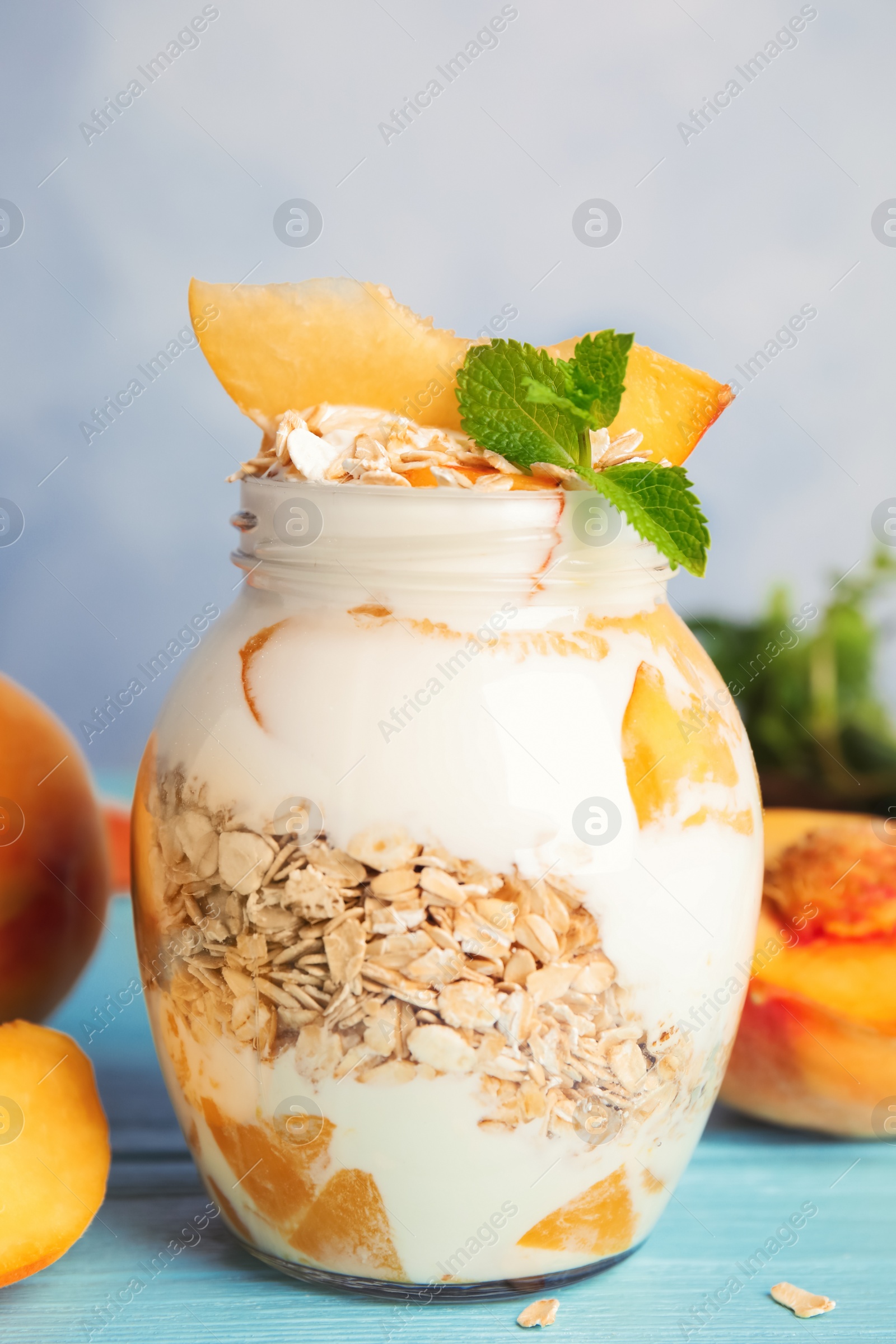 Photo of Tasty peach dessert with yogurt and granola on light blue wooden table