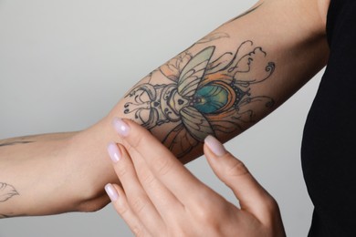 Photo of Woman applying cream on her arm with tattoos against light background, closeup