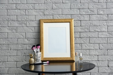 Photo of Mockup of blank frame and makeup brushes on table