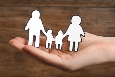 Woman holding paper family cutout on wooden background, closeup