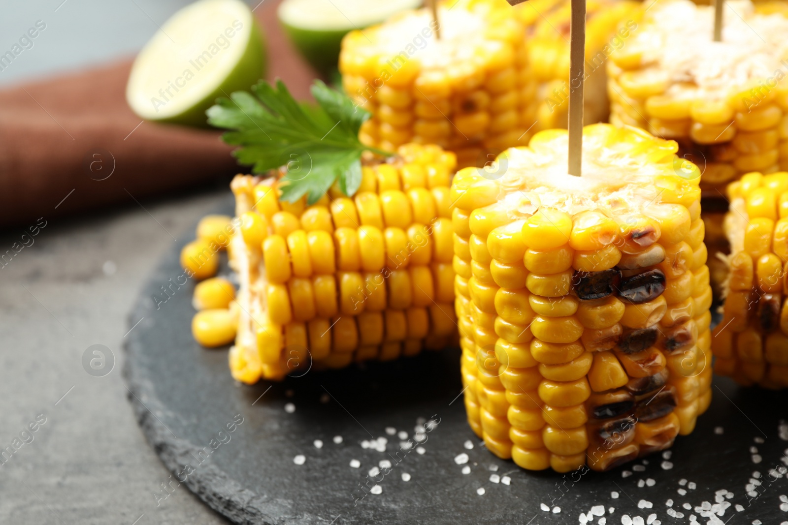Photo of Tasty grilled corn on black plate, closeup