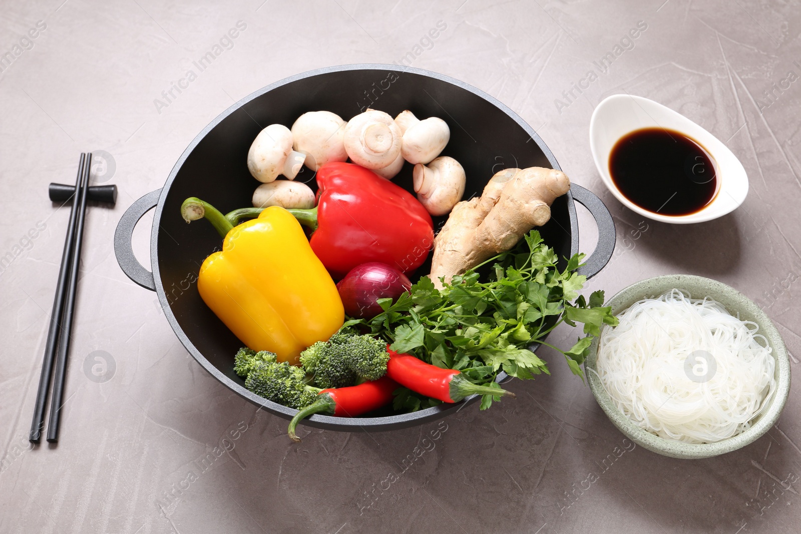 Photo of Wok, chopsticks and different products on grey textured table