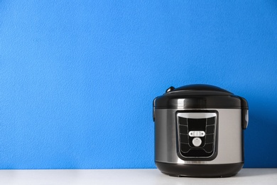 Photo of Modern multi cooker on table near color wall, space for text