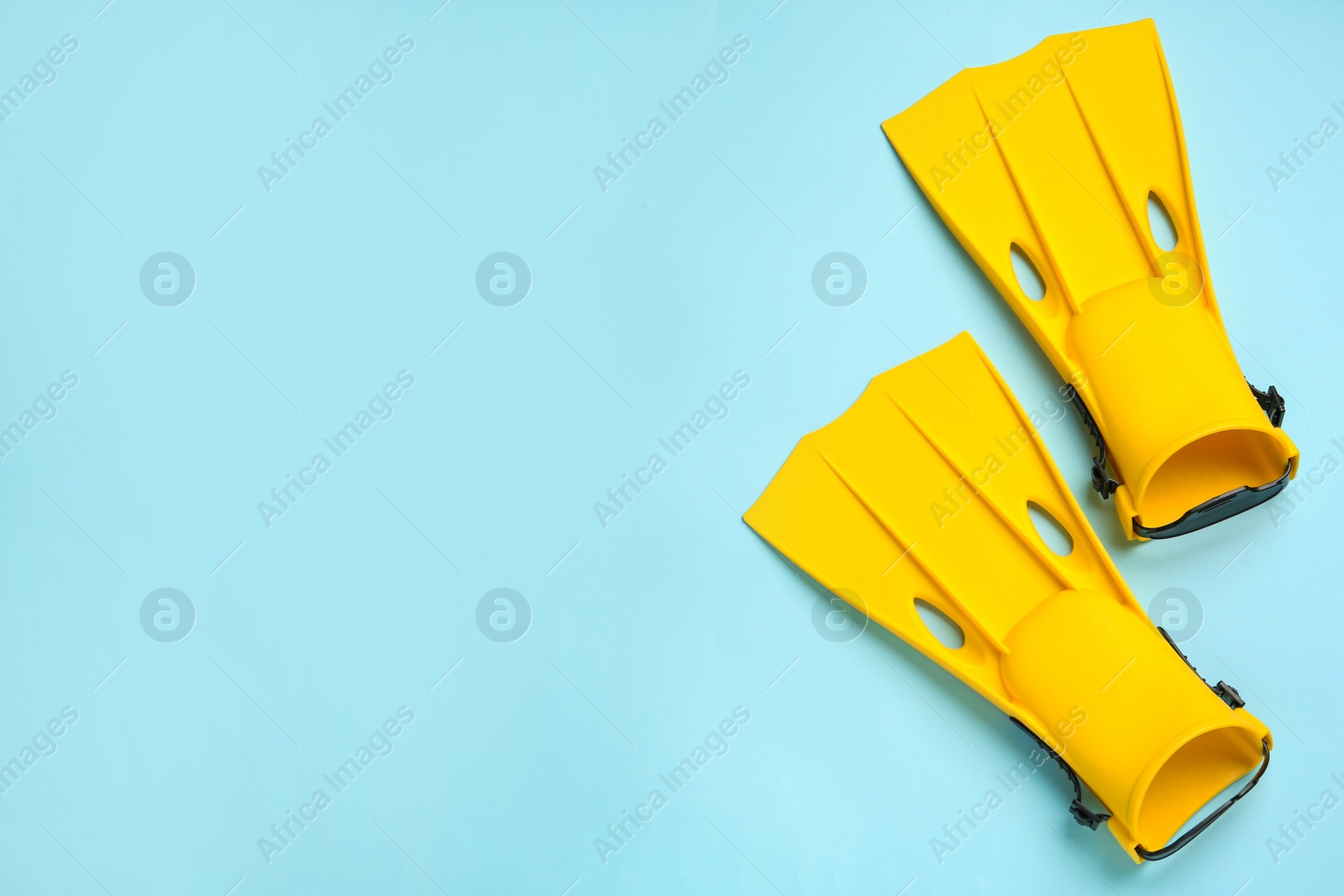 Photo of Pair of yellow flippers on light blue background, flat lay. Space for text
