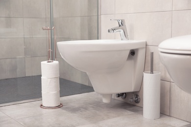 Holder with toilet paper rolls on floor in bathroom