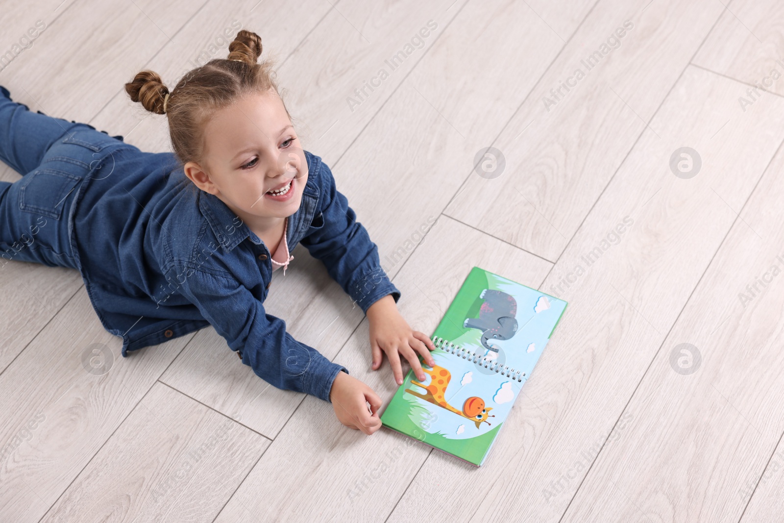 Photo of Cute little girl with book on warm floor at home, space for text. Heating system