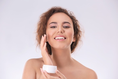 Beautiful young woman with problem skin applying anti acne cream on light background