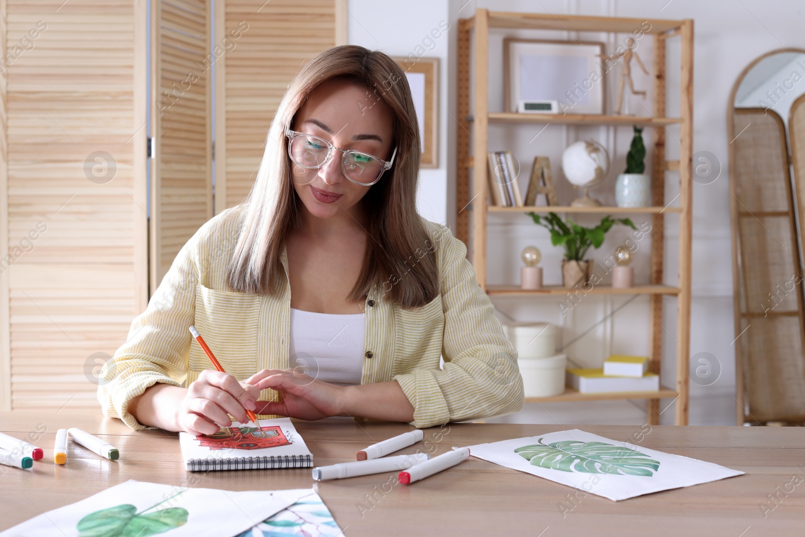 Photo of Young woman drawing in sketchbook with pencil at wooden table indoors