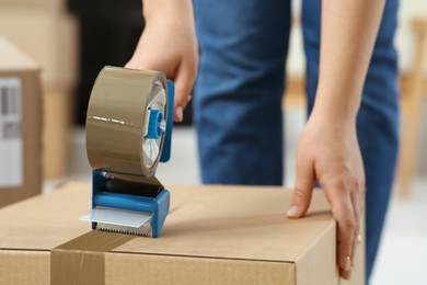 Photo of Woman applying adhesive tape on box with dispenser indoors, closeup