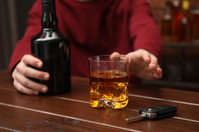 Man reaching for alcoholic drink at table with car keys, closeup. Don't drink and drive concept