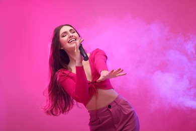 Photo of Emotional woman with microphone singing on pink background. Space for text