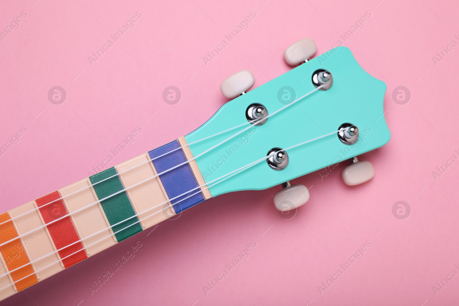 Photo of Colorful ukulele neck on pink background, top view. String musical instrument