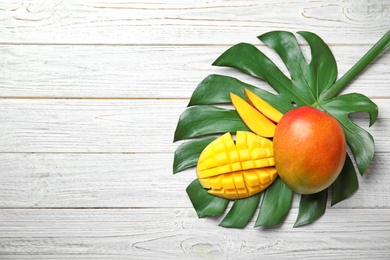 Photo of Flat lay composition with ripe mangoes, monstera leaf and space for text on white wooden background