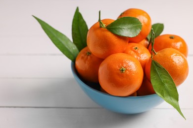 Photo of Fresh ripe juicy tangerines and green leaves in bowl on white wooden table, closeup. Space for text
