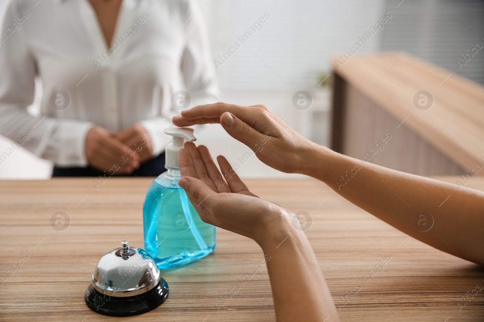 Photo of Woman applying antiseptic gel at hotel reception, closeup