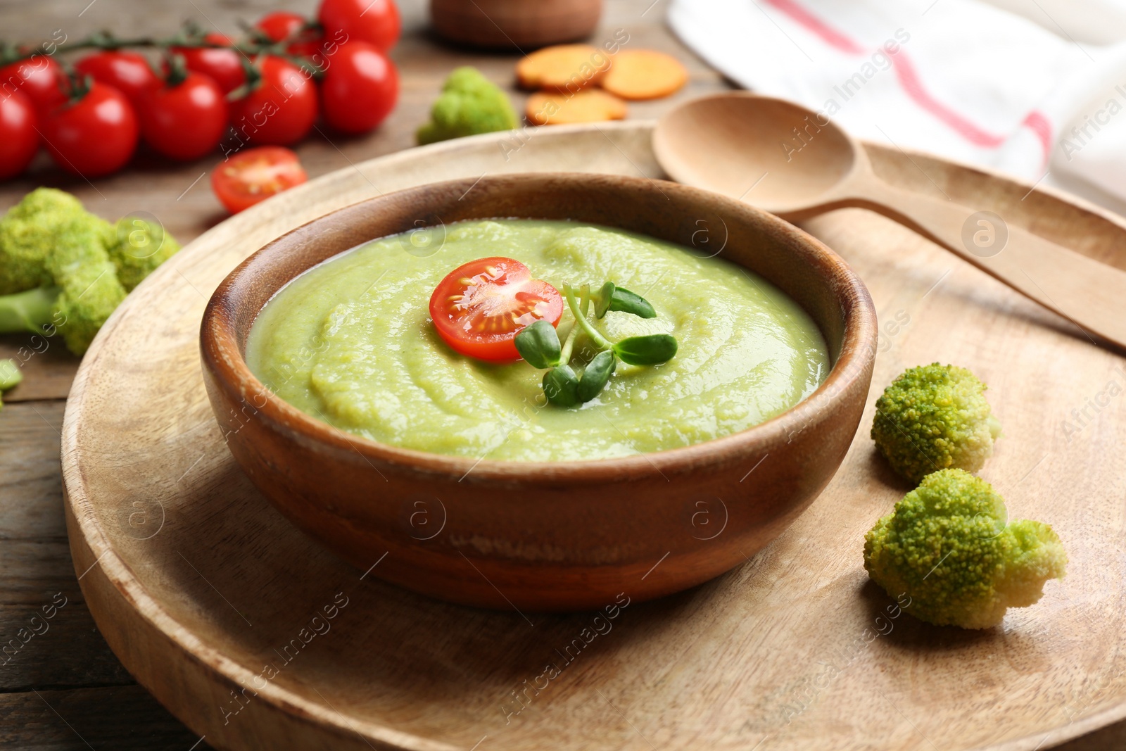 Photo of Bowl of broccoli cream soup with tomato and microgreens served on wooden tray