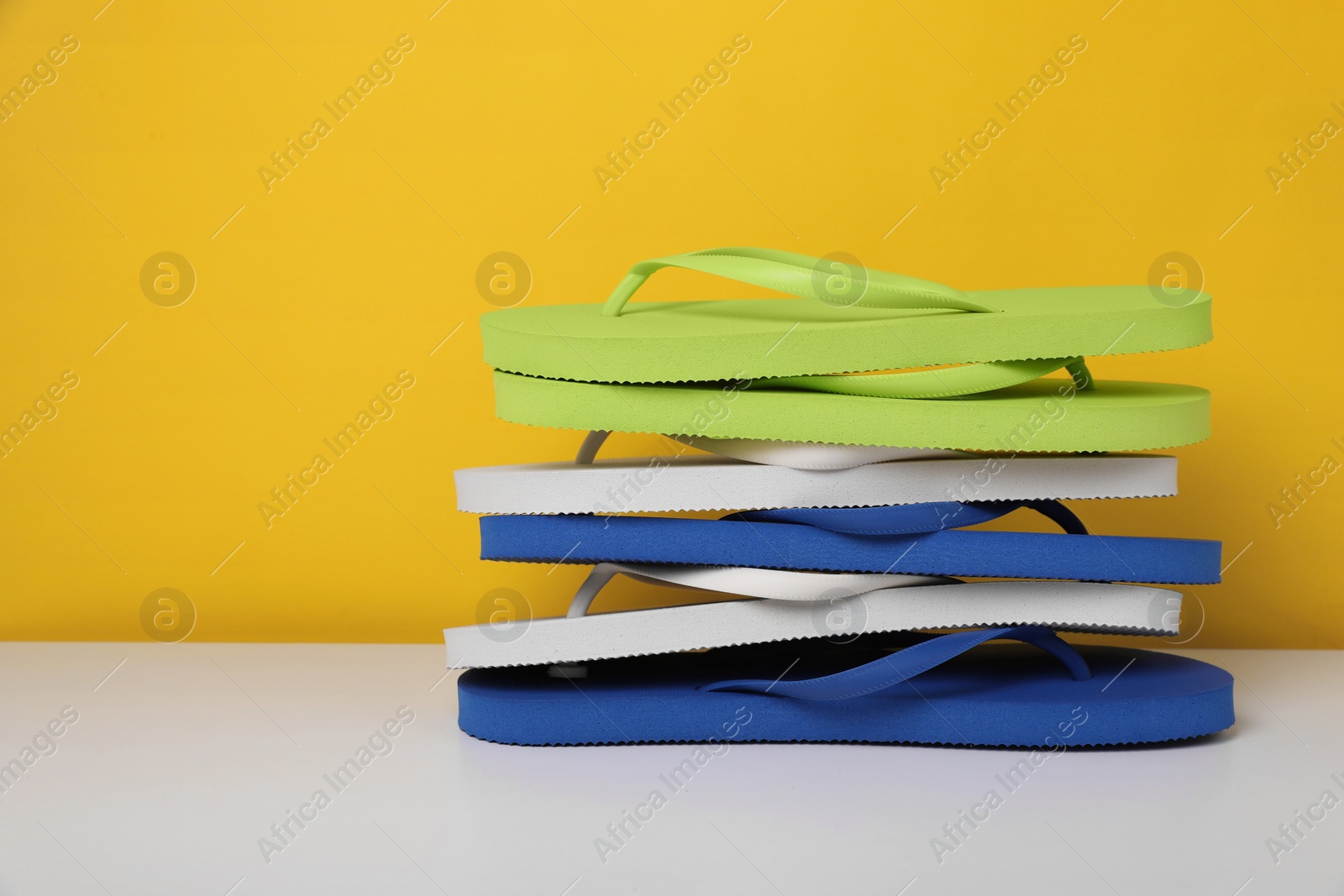 Photo of Stack of different flip flops on white table against yellow background