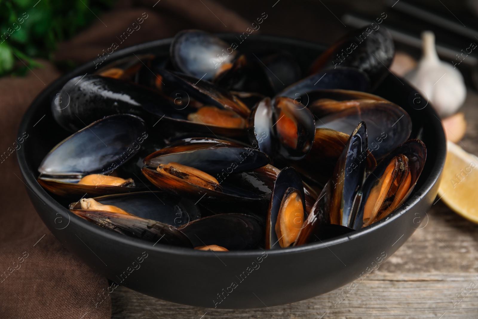 Photo of Bowl of delicious cooked mussels on table, closeup