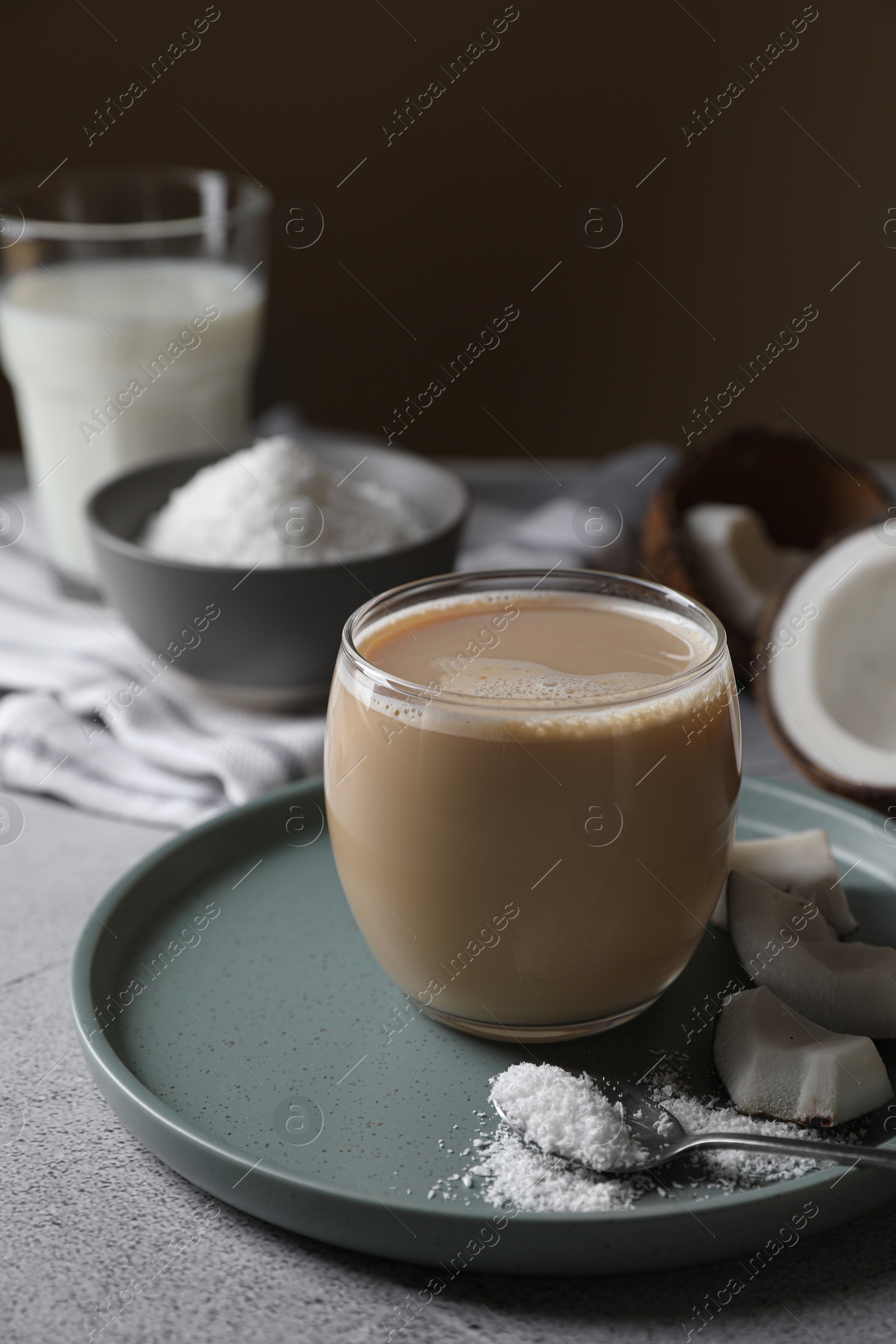 Photo of Glass of coffee with coconut milk, pieces and flakes on light grey table, space for text