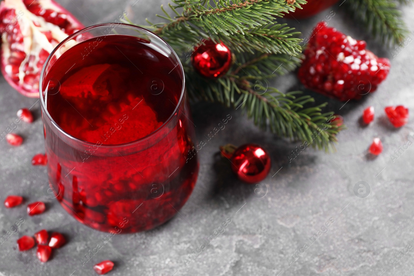 Photo of Aromatic Sangria drink in glass, Christmas decor and pomegranate grains on grey textured table