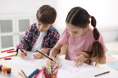 Happy brother and sister drawing at white table in room