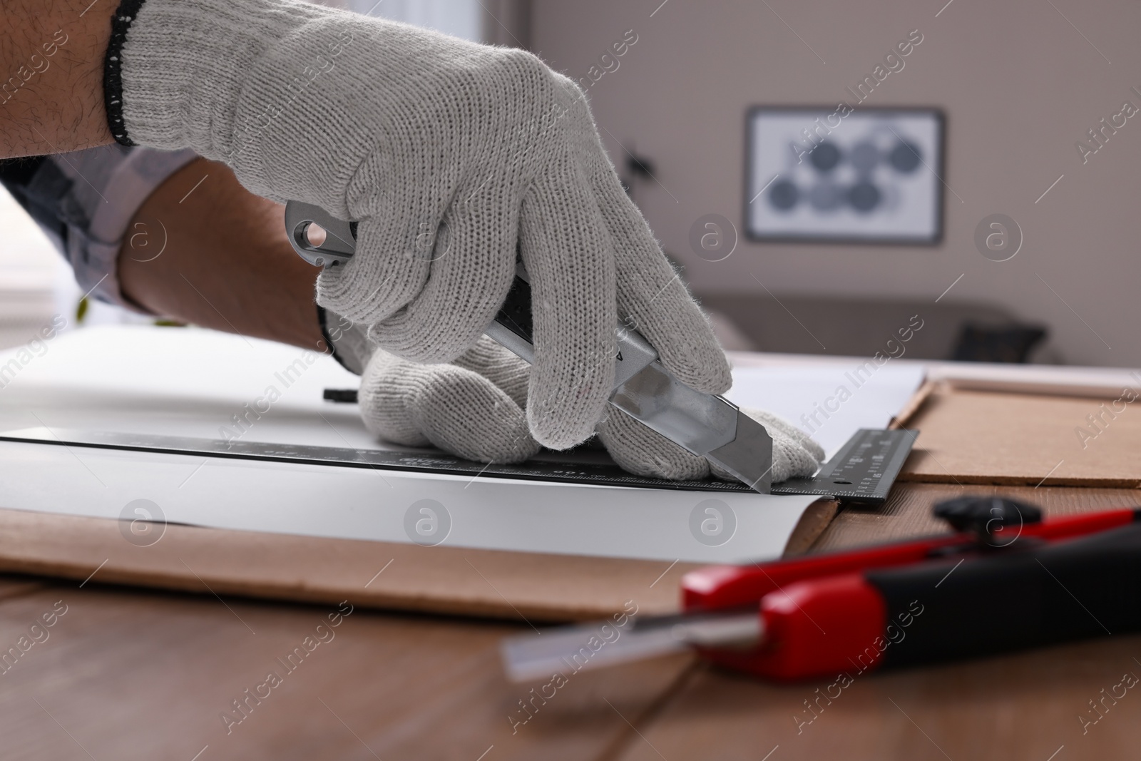 Photo of Worker cutting paper with utility knife and ruler at wooden table indoors, closeup