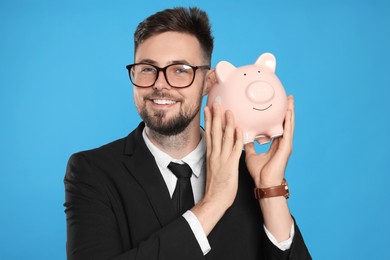 Happy businessman with piggy bank on light blue background