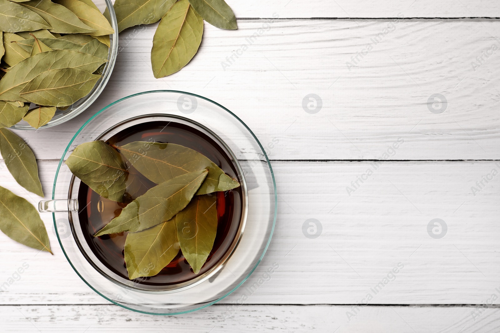 Photo of Cup of freshly brewed tea with bay leaves on white wooden table, flat lay. Space for text