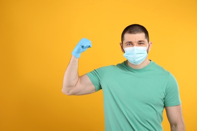 Photo of Man with protective mask and gloves showing muscles on yellow background, space for text. Strong immunity concept