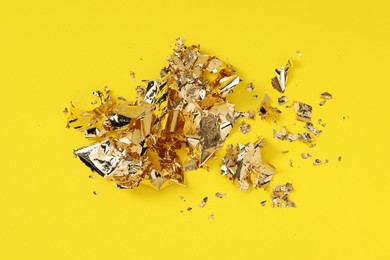 Photo of Many pieces of edible gold leaf on yellow background, above view