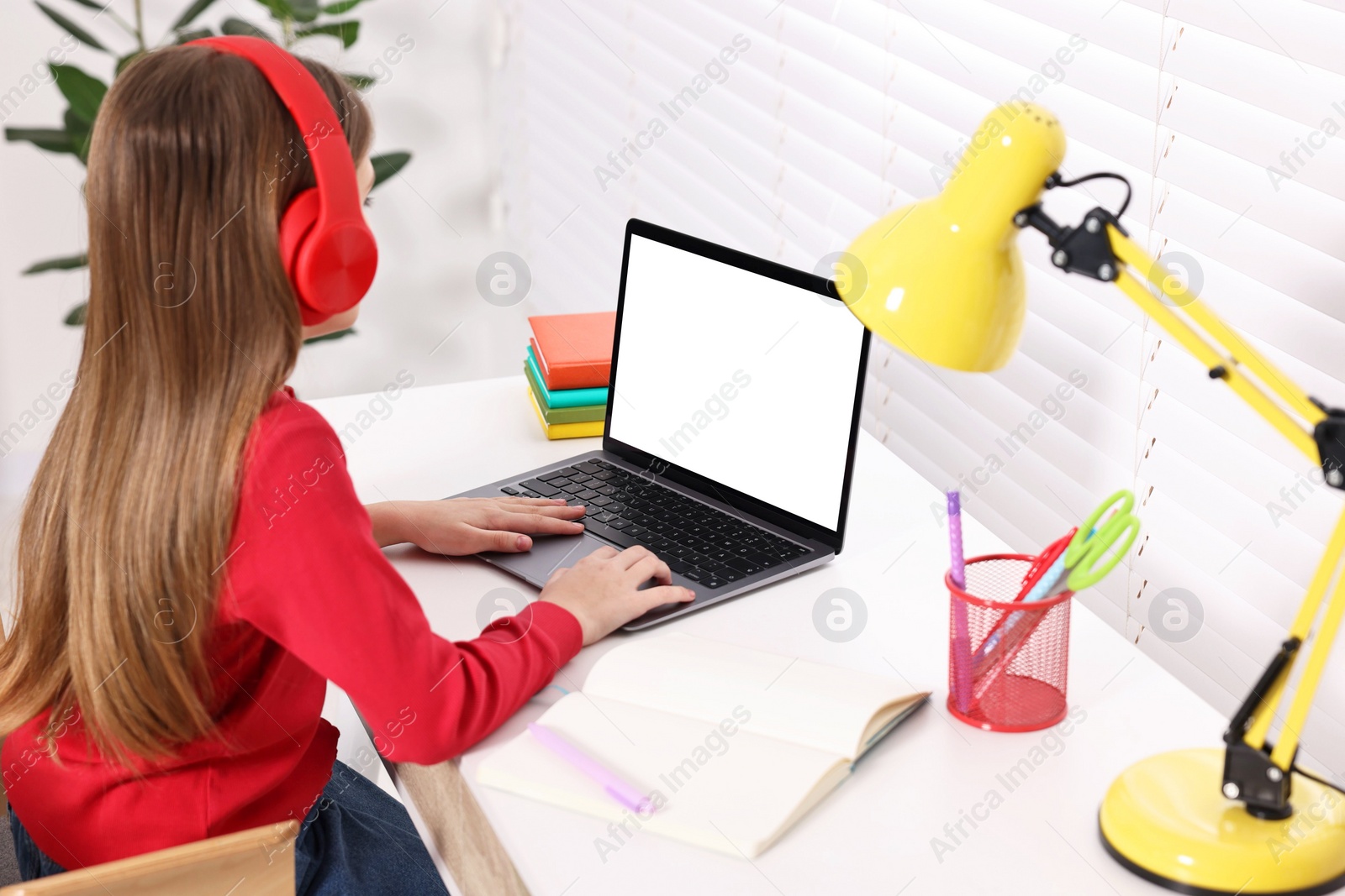 Photo of E-learning. Girl using laptop and headphones during online lesson at table indoors