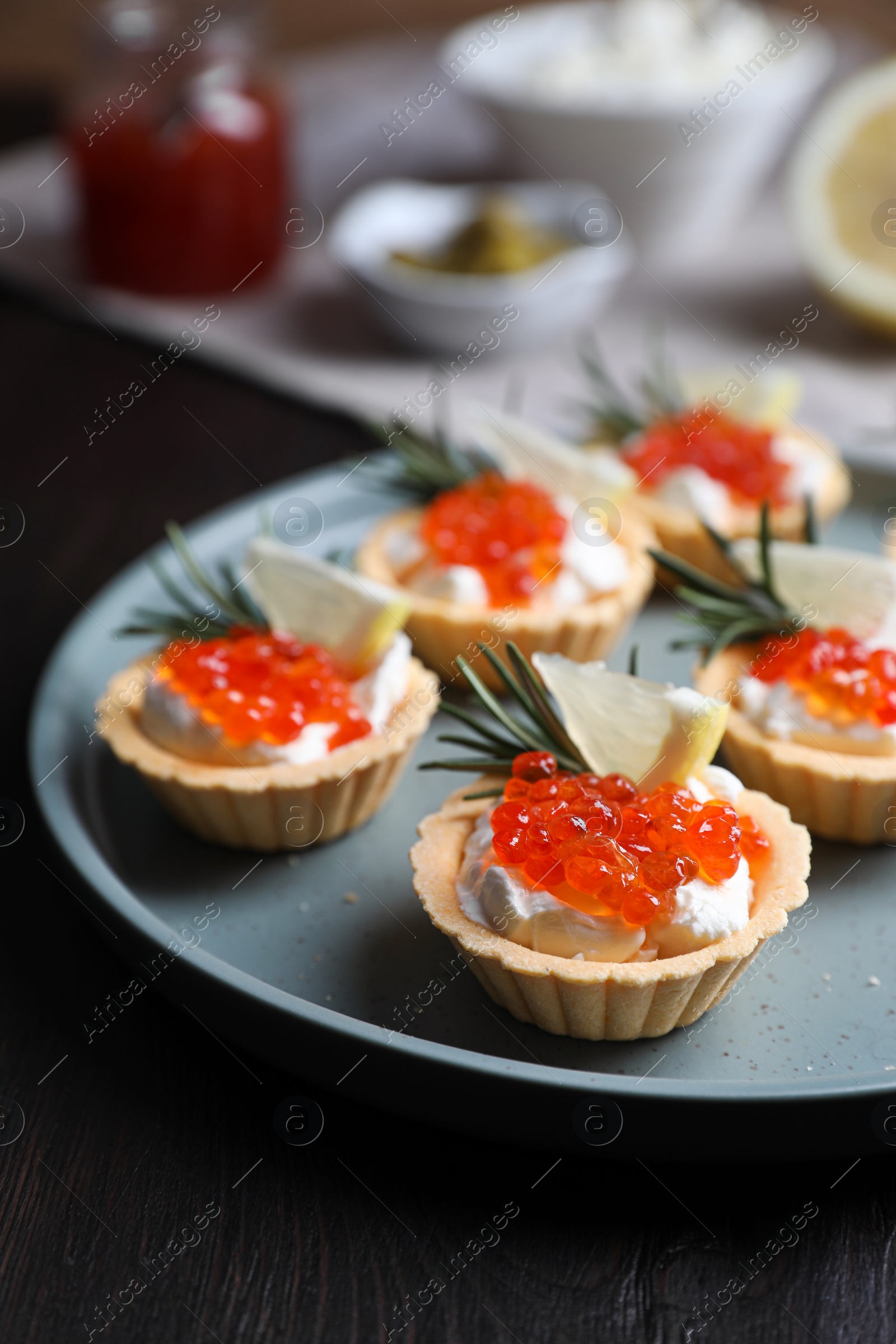 Photo of Delicious tartlets with red caviar and cream cheese served on wooden table, closeup