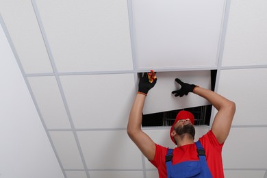 Photo of Electrician with pliers repairing ceiling light indoors, low angle view. Space for text