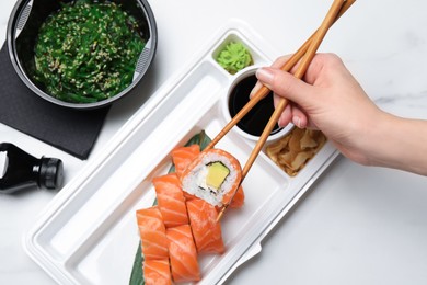 Photo of Woman eating sushi rolls with chopsticks at white table, top view