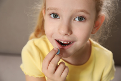 Photo of Little girl taking vitamin pill at home, closeup
