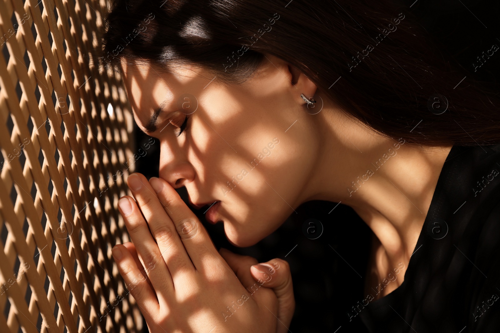 Photo of Woman praying to God during confession in booth, closeup