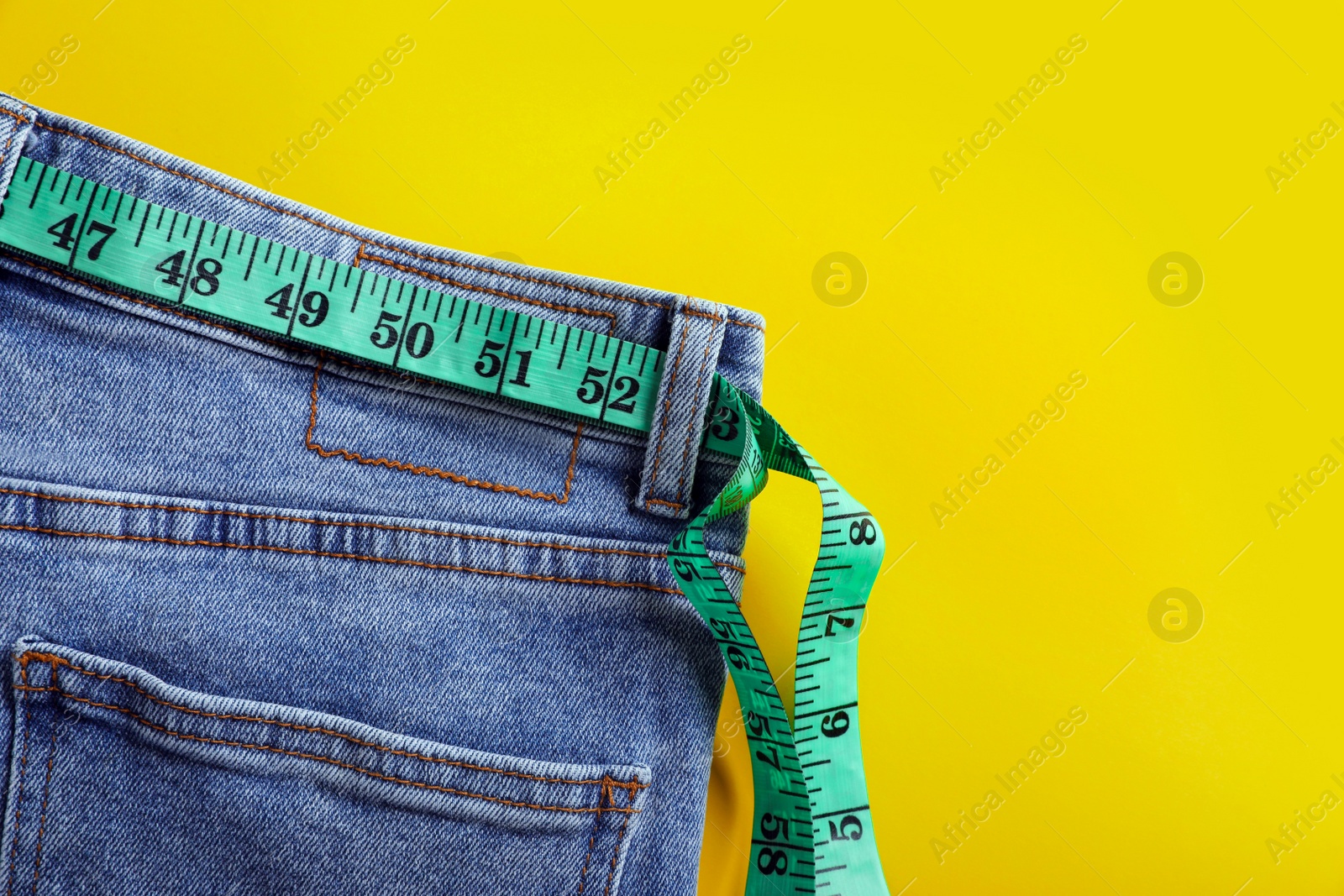 Photo of Jeans with measuring tape on yellow background, top view and space for text. Weight loss concept