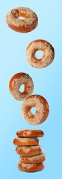 Image of Many fresh bagels with sesame seeds falling onto stack on light blue background