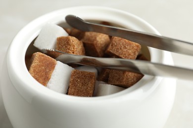 Photo of Different refined sugar cubes in bowl on light table, closeup