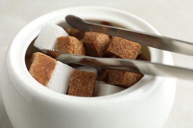 Different refined sugar cubes in bowl on light table, closeup