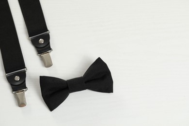 Photo of Stylish black bow tie and suspenders on white wooden table, flat lay. Space for text