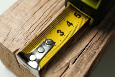 Photo of Tape measure on timber strip, closeup. Construction tool