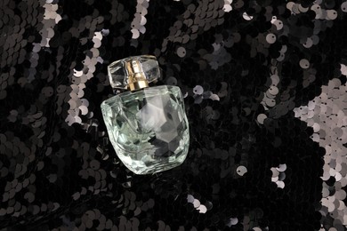 Luxury perfume in bottle on fabric with shiny sequins, above view