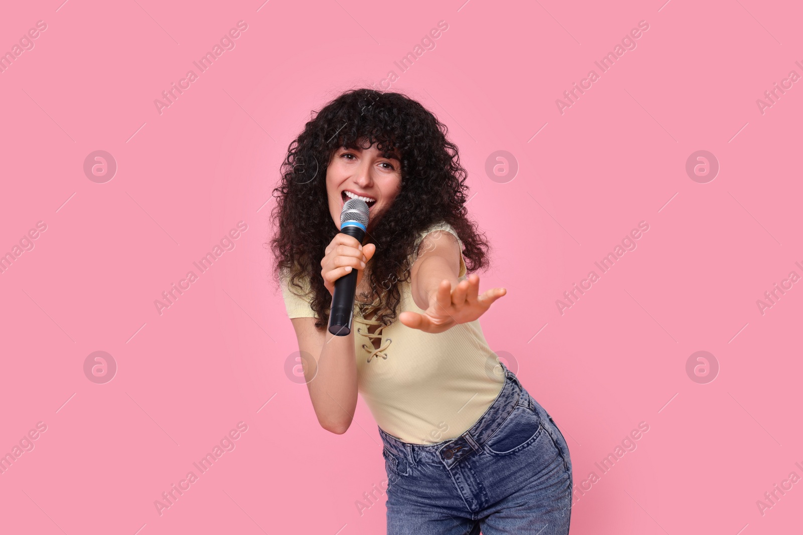 Photo of Beautiful young woman with microphone singing on pink background