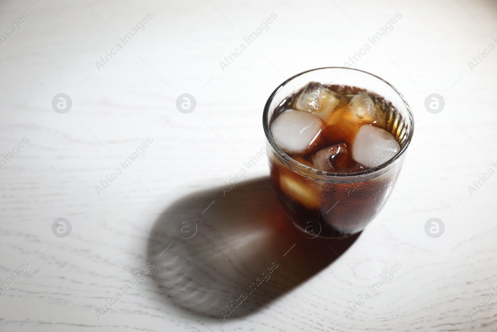 Photo of Refreshing iced coffee in glass on white wooden table. Space for text